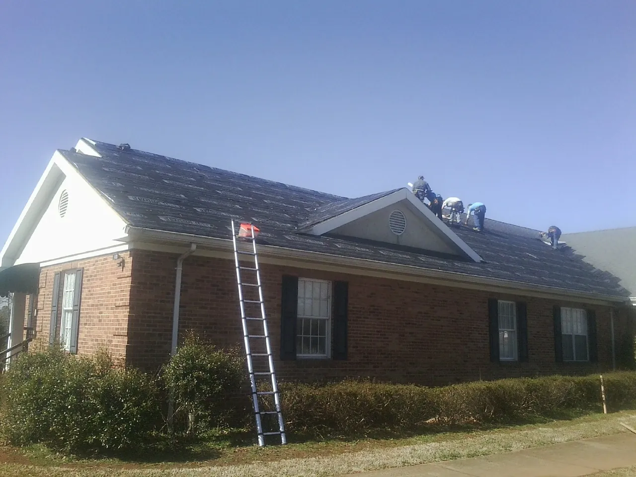 Crew tearing shingles off a brick ranch roof with a ladder set — Emergency Roof Repair work by our crew in Liberty