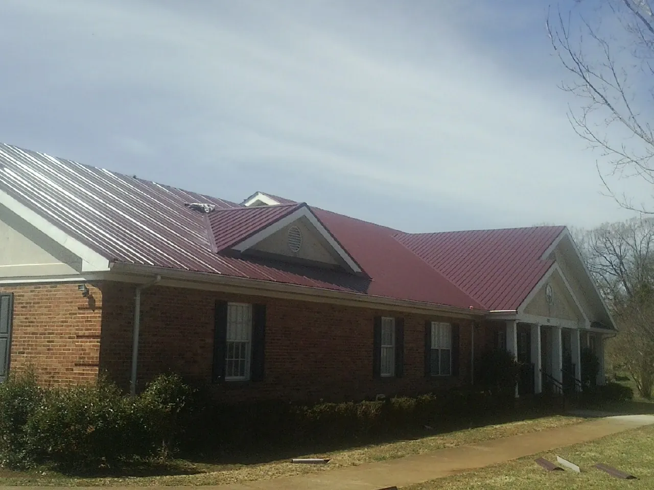 Red metal roof with gabled entries on a long brick building, from a Hail Damage Roof Repair job in Liberty
